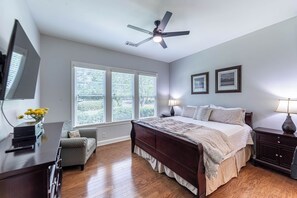 Ein Schlafzimmer mit einem Bett, einem Schreibtisch, einem Stuhl, einem Deckenventilator und zwei Fenstern mit Jalousien.