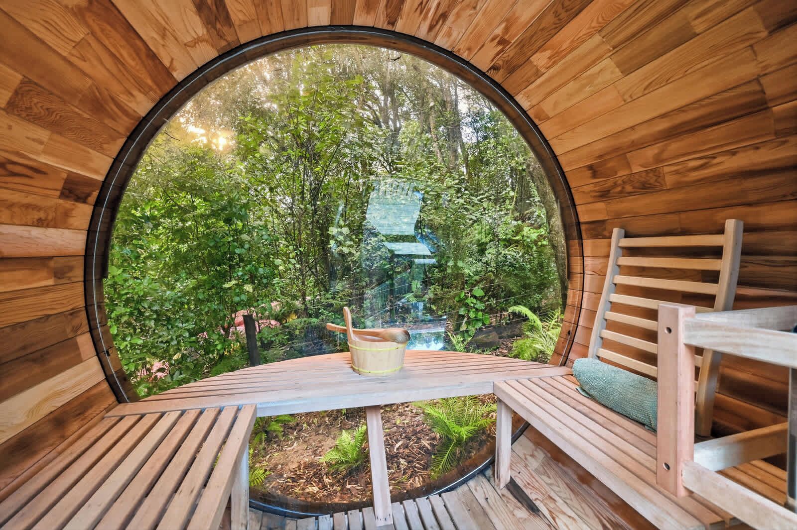 Une structure circulaire en bois, comprenant une table et des chaises, entourée d’une vue sur la forêt.