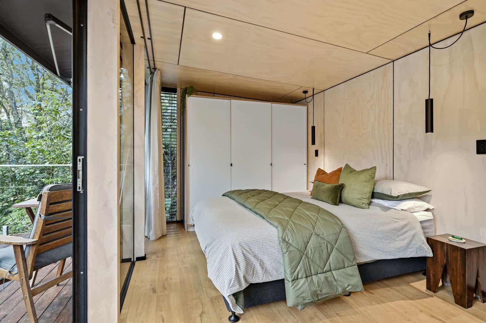 Ein modernes Schlafzimmer mit Bett, Nachttisch und Blick auf Grün.
