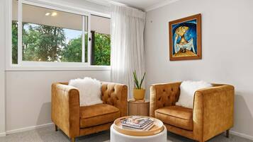 A room with two armchairs, a round coffee table, a painting, and a window with a view of trees.
