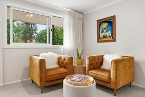 A room with two armchairs, a round coffee table, a painting, and a window with a view of trees.