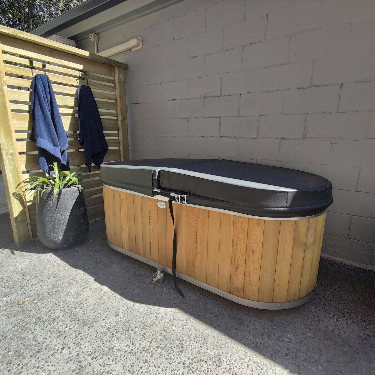 A hot tub with a wooden exterior, a potted plant, and a wooden fence with clothes hanging on it.