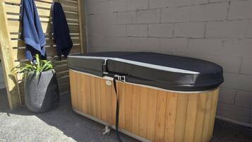 A hot tub with a wooden exterior, a potted plant, and a wooden fence with clothes hanging on it.