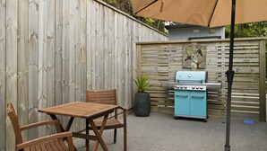 An outdoor patio with a wooden table and chairs, a grill, and a potted plant.