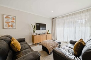 A living room with two leather sofas, a wooden console table, and a large window with sheer curtains.
