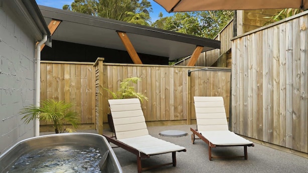 A backyard with a hot tub, two lounge chairs, and a wooden fence.