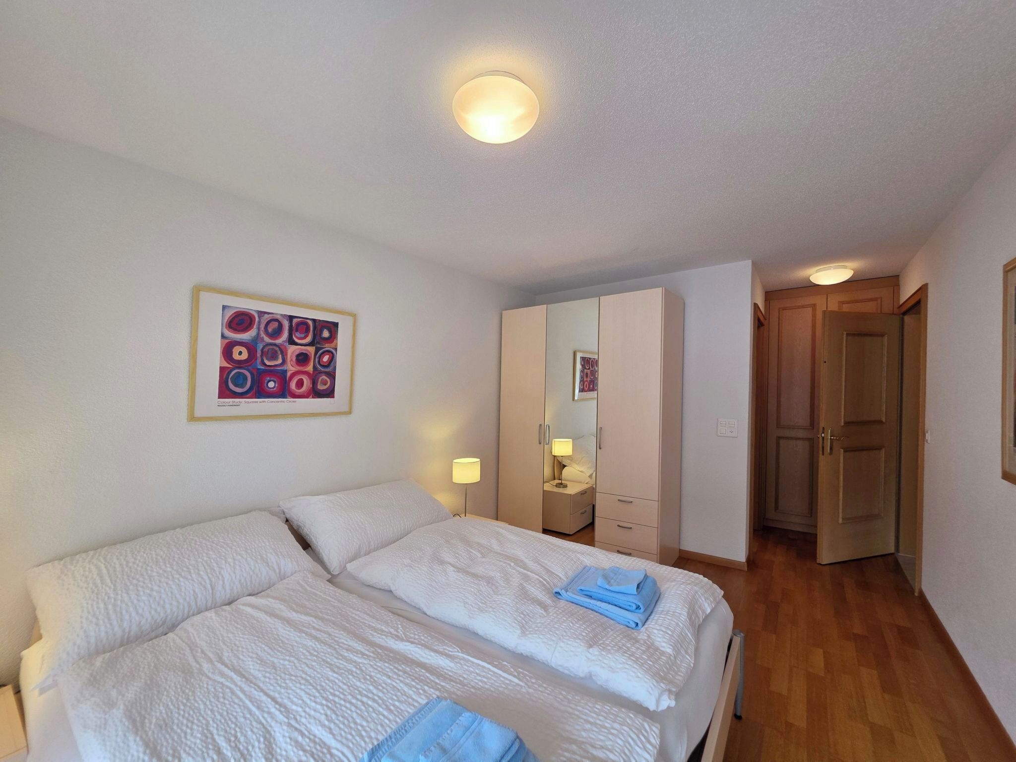 Een hotelkamer met twee bedden, een nachtkastje met een lamp, een kledingkast en een deur naar een andere kamer.