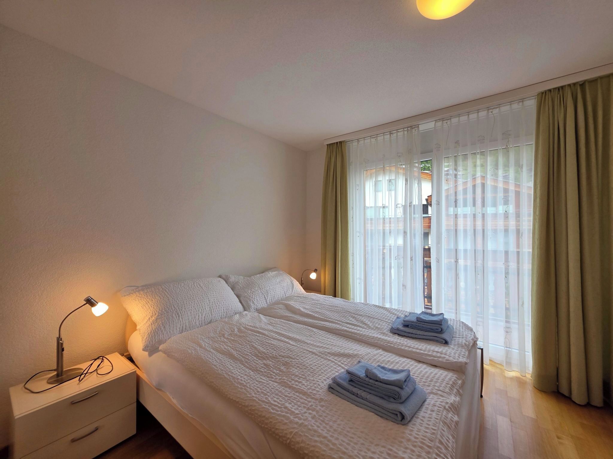 A hotel room with a bed, bedside lamps, a nightstand, and a window with curtains.