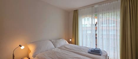 Una habitación de hotel con cama, lámparas de noche, mesita de noche y una ventana con cortinas.