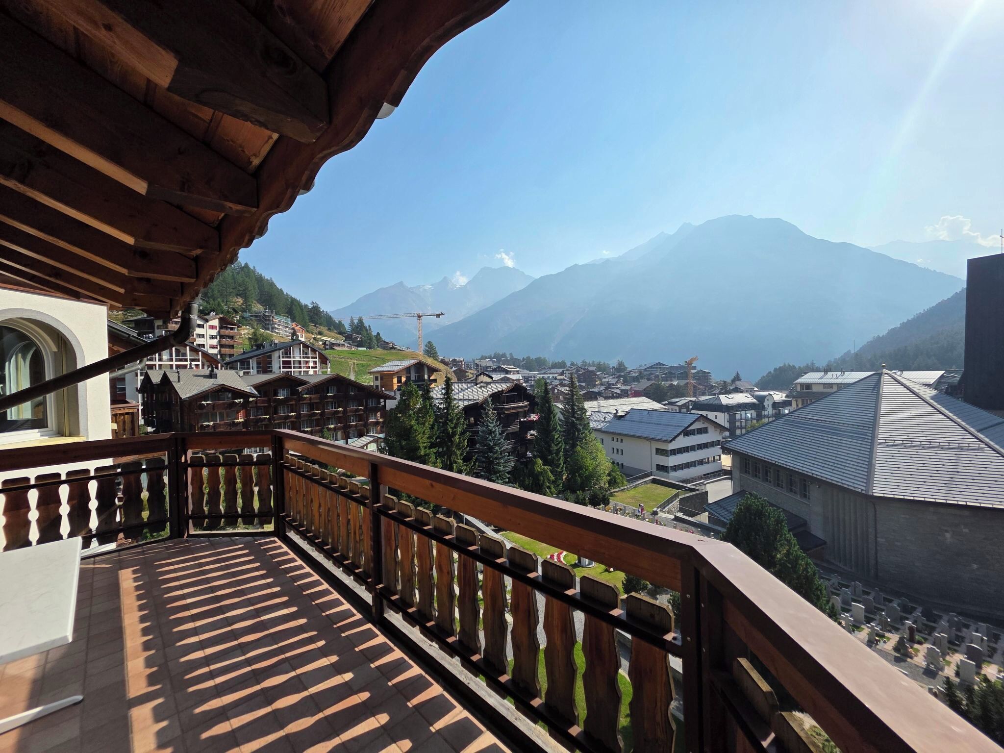 A balcony with a view of a mountain town, wooden railings, and a clear sky.