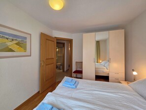 Ein Hotelzimmer mit Bett, Stuhl, Kleiderschrank und einem durchgegangenen Tür sichtbaren Badezimmer.