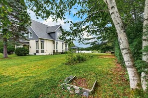 Une maison à deux étages, dotée d’un toit en pente, entourée d’une pelouse bien entretenue et d’arbres.