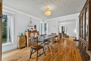 Un vaste espace dédié à la salle à manger, avec une table et des chaises en bois, un lustre et une vue sur l’extérieur.
