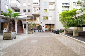 A multi-level building with a covered outdoor area, bicycles, and a palm tree. - Cocon Lumineux Saint-Antoine - Welkeys (Paris)