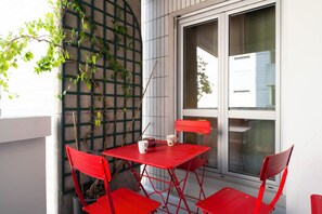 Ein rotes Metall-Tisch- und Stuhlgarnitur steht vor einem Gebäude mit einem Fenster und einer mit Kletterpflanzen bewachsenen Mauer.