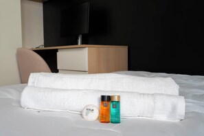 Ein Hotelzimmer mit einem Bett, einem Fernseher, einem Nachttisch aus Holz und zwei Shampoo-Flaschen.