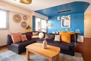 A modern living room with a sectional sofa, a wooden coffee table, and a dining area with a table set for four. - Cocon Lumineux Saint-Antoine - Welkeys (Paris)