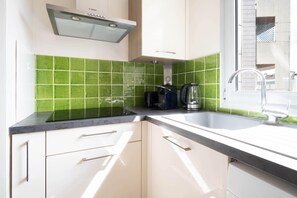 A kitchen with a Bosch range hood, green tiles, a sink, and a window. - Cocon Lumineux Saint-Antoine - Welkeys (Paris)