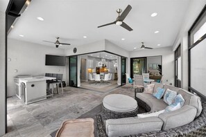 Ein modernes Wohnzimmer mit Sofa, Hocker und einem Essbereich mit Tisch und Stühlen.