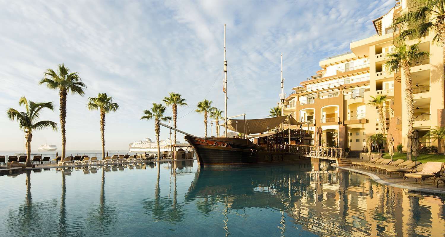 A pool area with a ship, palm trees, and a hotel building.