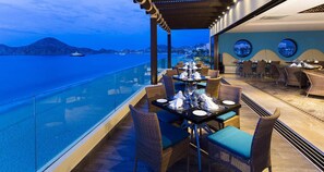 A dining area with tables set for guests, overlooking a body of water and a distant coastline. - Beach Resort Del Arco with Breathtaking Oceanviews (Cabo San Lucas)