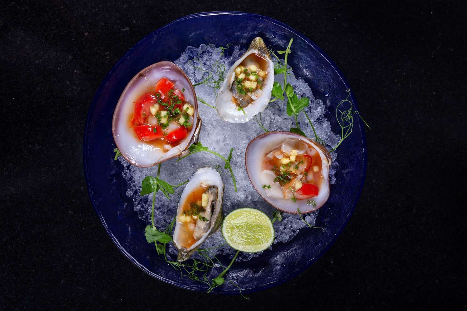 A plate with four oysters on ice, garnished with herbs and a slice of lime.