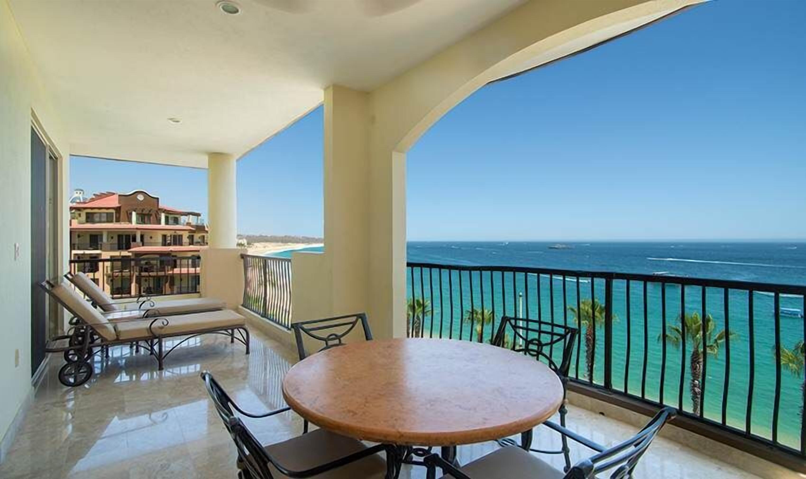 Ein Balkon mit Tisch und Stühlen, Blick auf das Meer und ein Gebäude im Hintergrund.