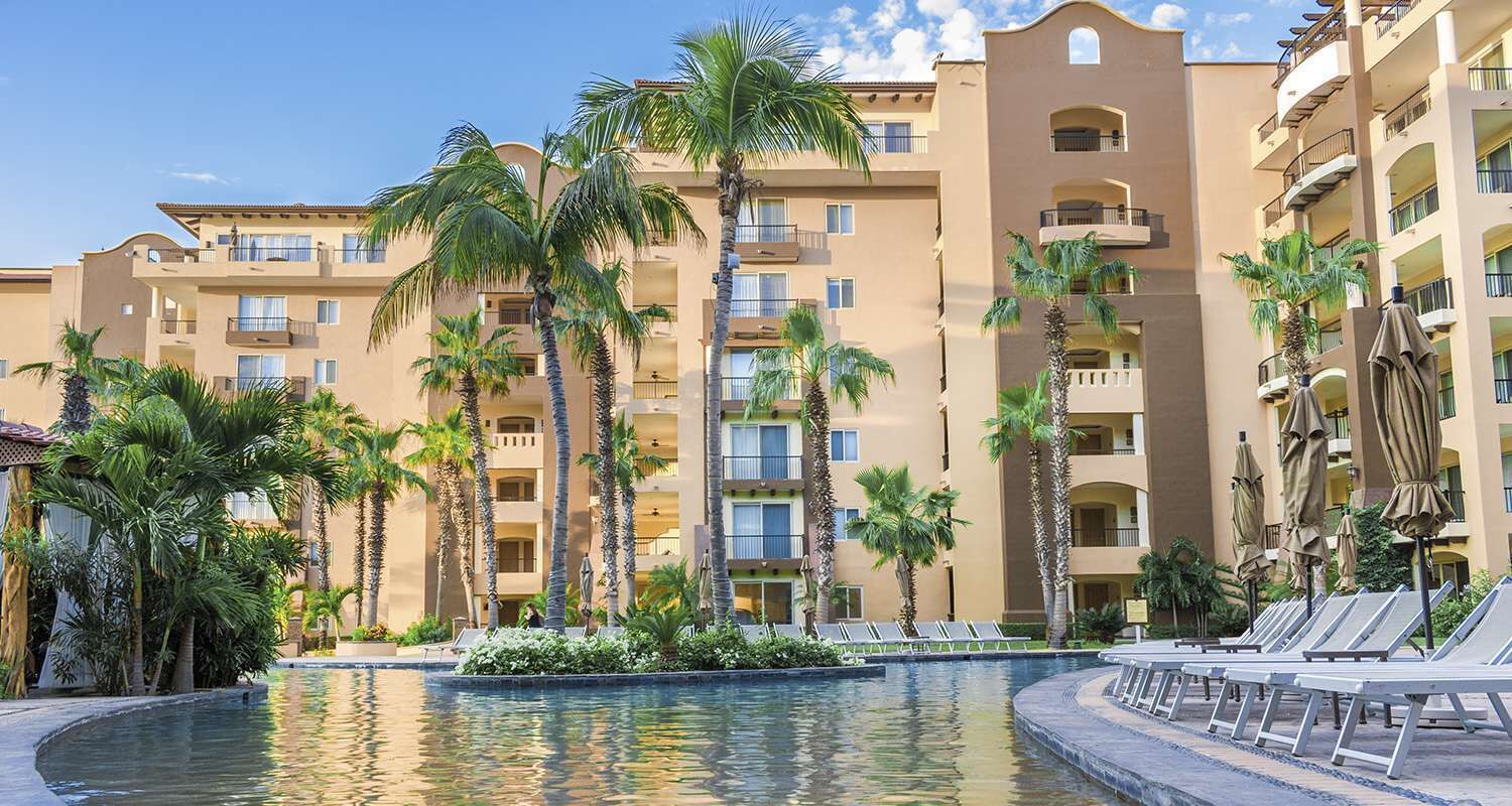 A hotel with a swimming pool, palm trees, and lounge chairs.