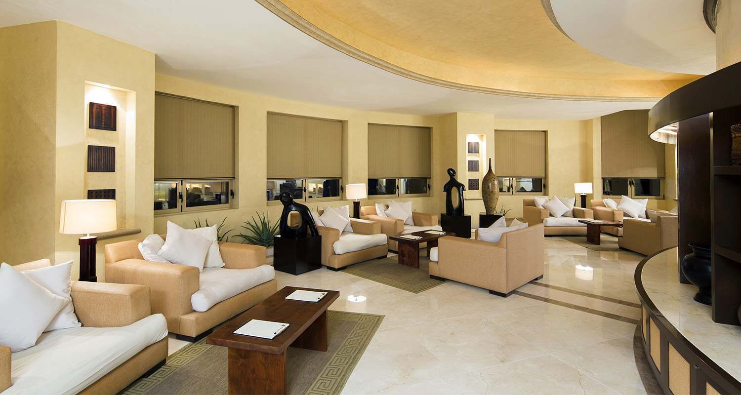 A spacious hotel lobby with multiple seating areas, a reception desk, and a large vase.