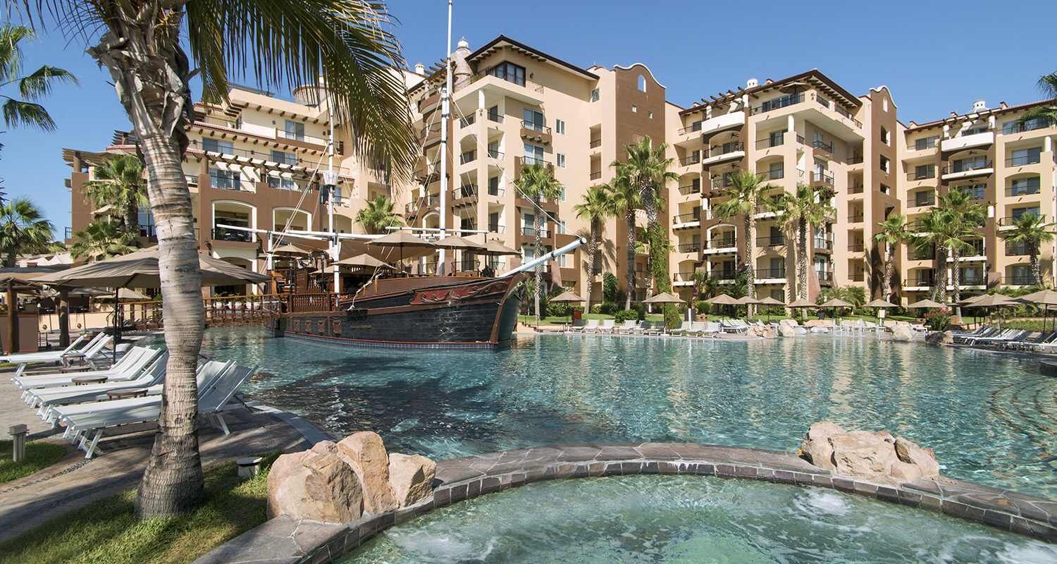 Un resort con piscina, palmeras y una estructura con forma de barco.