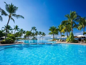 Una grande piscina all'aperto con acqua cristallina, circondata da palme e lettini da relax.