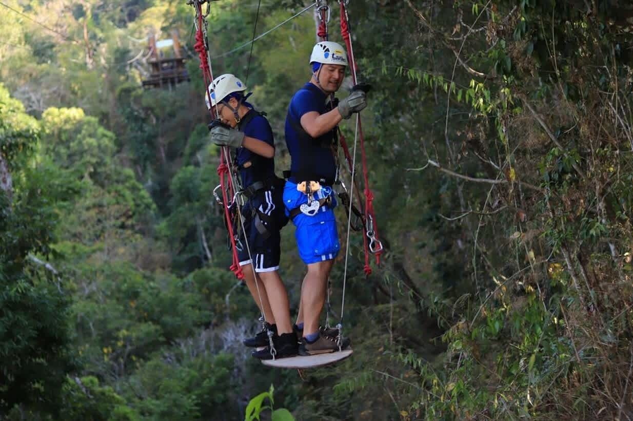 Zwei Personen auf einer Zipline durch ein bewaldetes Gebiet.