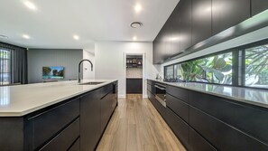 A modern kitchen with a central island, dark cabinetry, and a view of greenery through large windows. - Tranquility On Invermay (Tomerong)