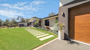A modern house with a well-maintained lawn, a driveway leading to a garage, and a variety of plants. - Tranquility On Invermay (Tomerong)