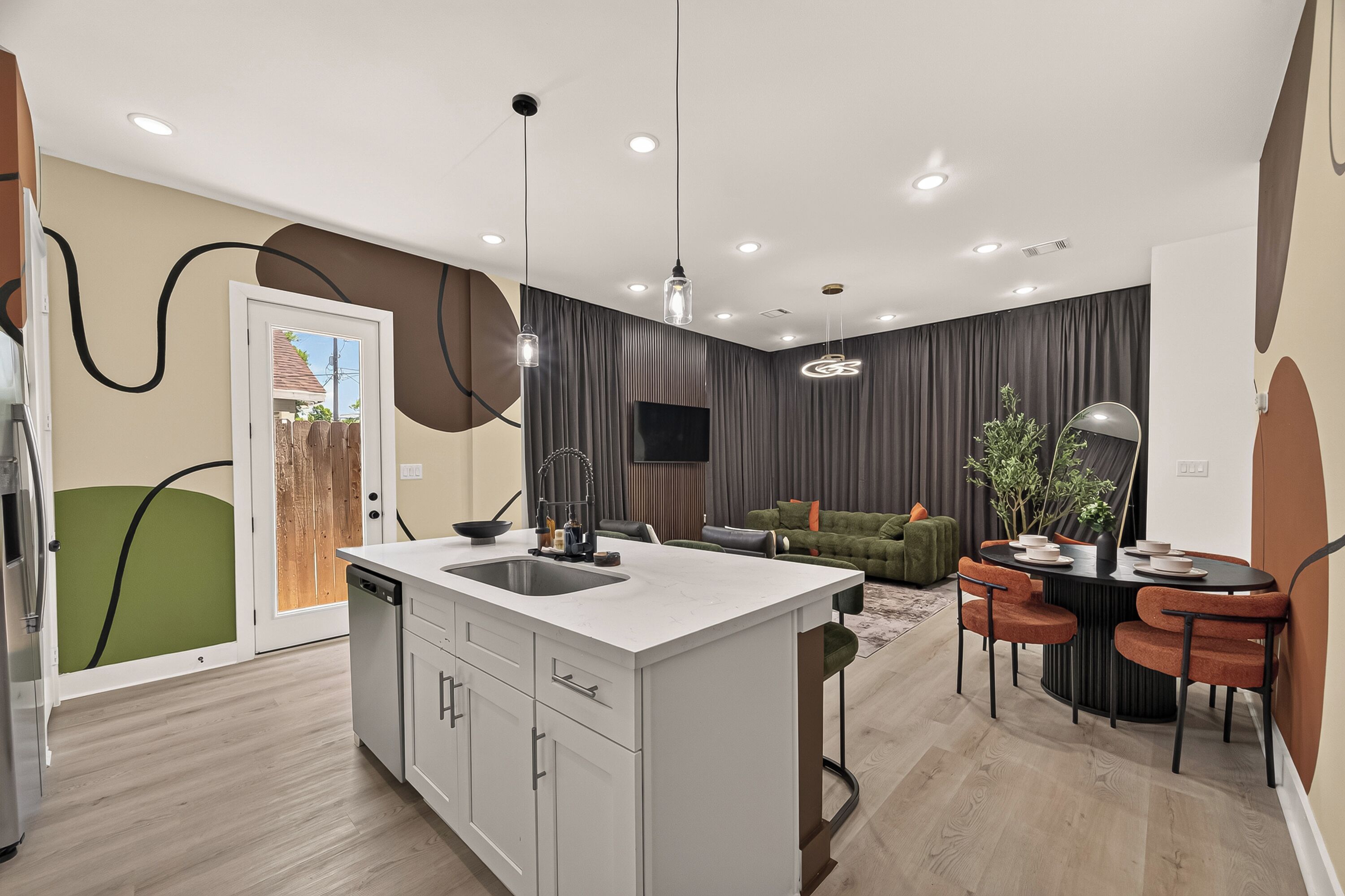 A modern kitchen with a central island, a dining area with a round table and chairs, and a living room with a sofa and a TV.
