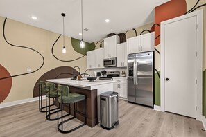 Eine moderne Küche mit weißen Schränken, Edelstahlgeräten, einer Bar mit grünen Stühlen und einem außergewöhnlichen Wanddesign.