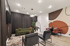 Ein modernes Wohnzimmer mit einem grünen Sofa, schwarzen Sesseln, einem Couchtisch und einem Essbereich mit einem runden Tisch und Stühlen.