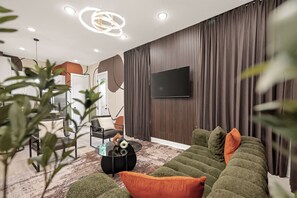 Ein modernes Wohnzimmer mit einer Eckcouch, einem Flachbildfernseher an einer Holzwand und einem Essbereich im Hintergrund.
