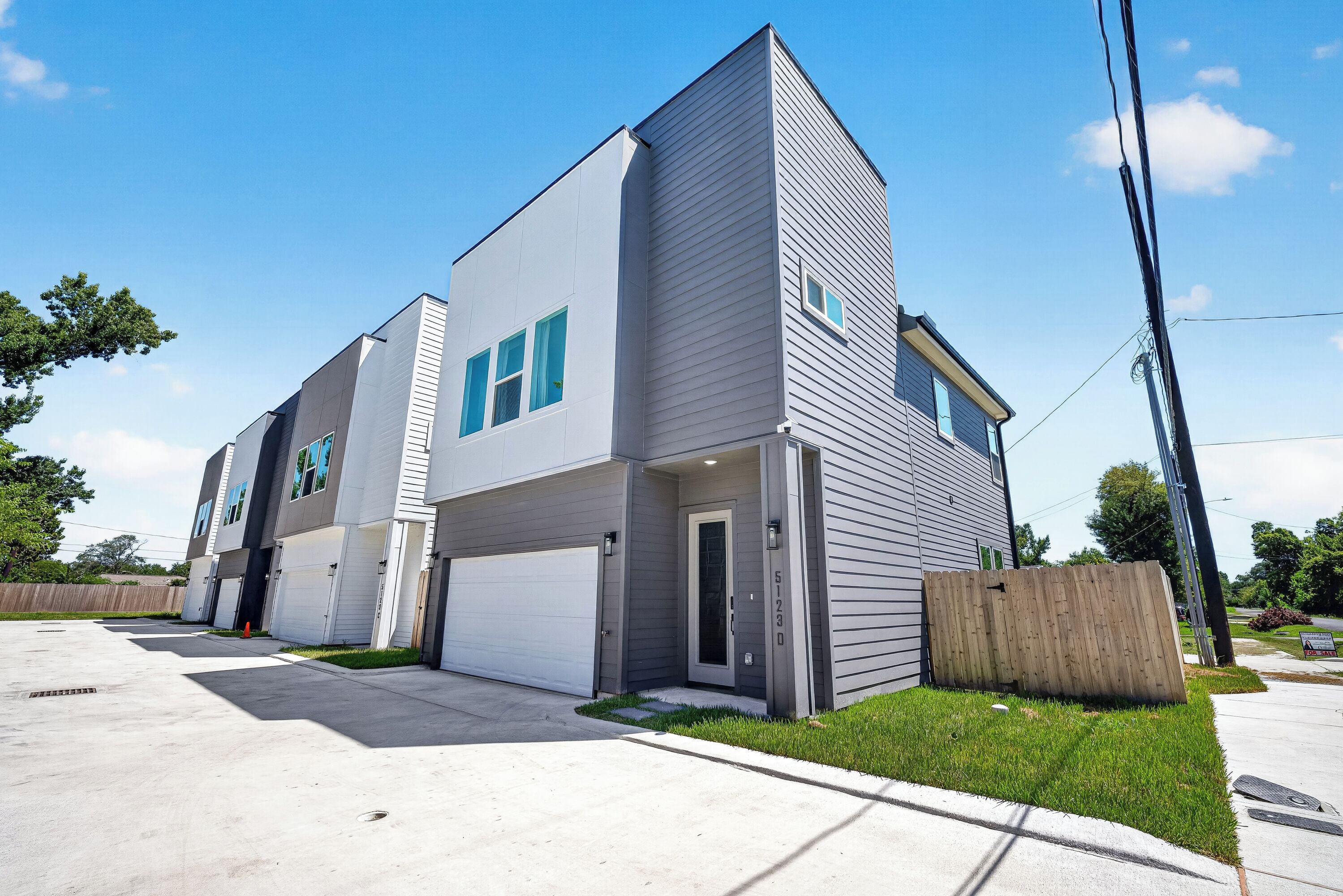 A modern two-story residential building with a garage, a front yard, and a wooden fence.