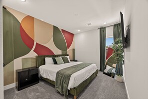 A modern bedroom with a bed, a nightstand, a wall-mounted TV, and a large window with curtains. - Stunning Designer Home Minutes to NRG, Medical Center & Downtown Sleeps 9 (Houston)