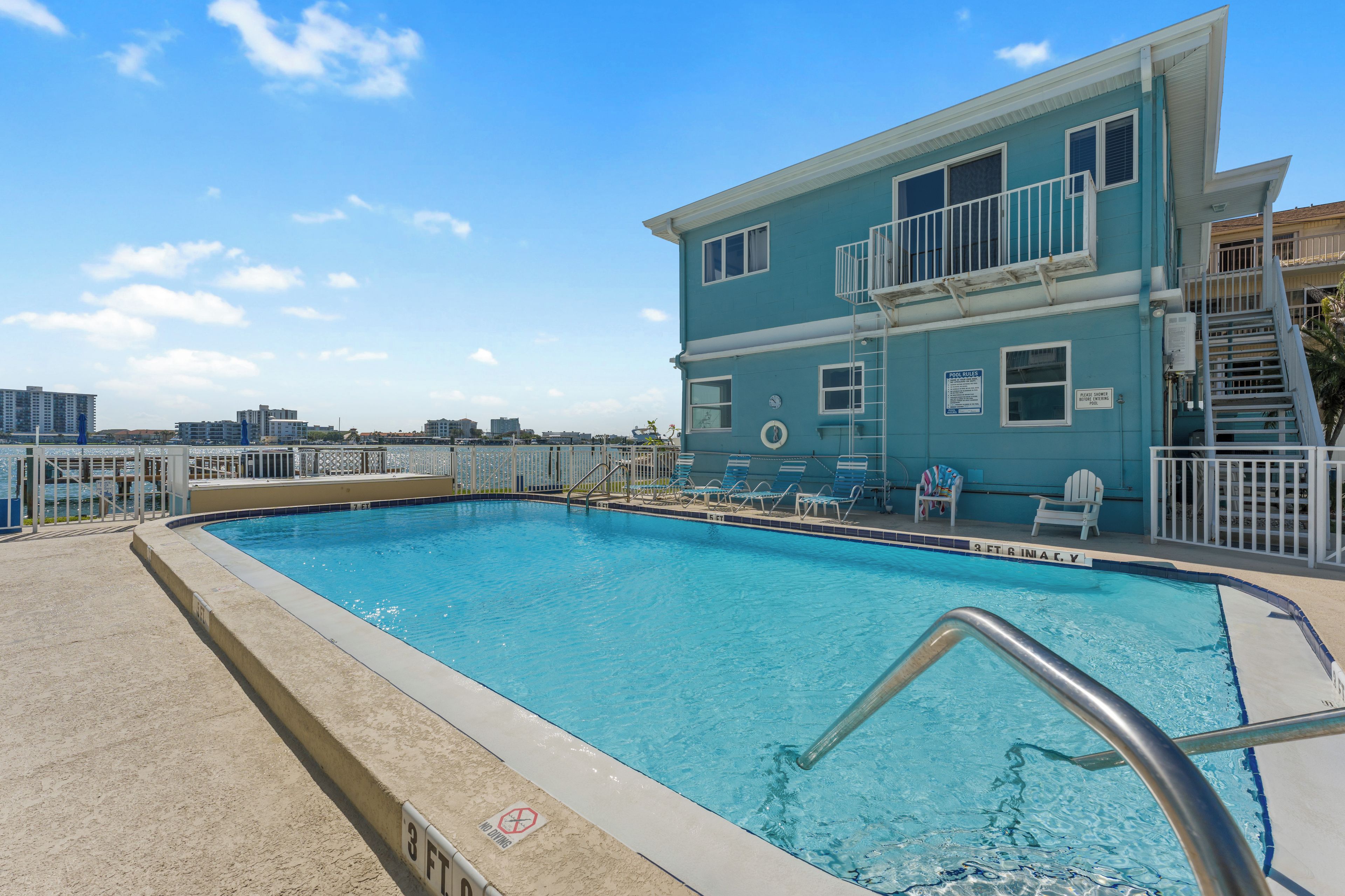 A swimming pool with a lifeguard stand, lounge chairs, and a building with a balcony.