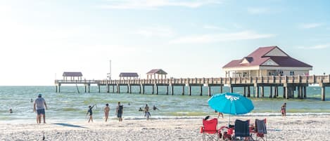 A beach with a pier, beach chairs, and a building with a red roof.