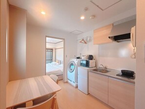 A compact hotel room with a kitchenette, a washing machine, and a bed. - Aoba Residence Designer Apartments 201 (大阪市)