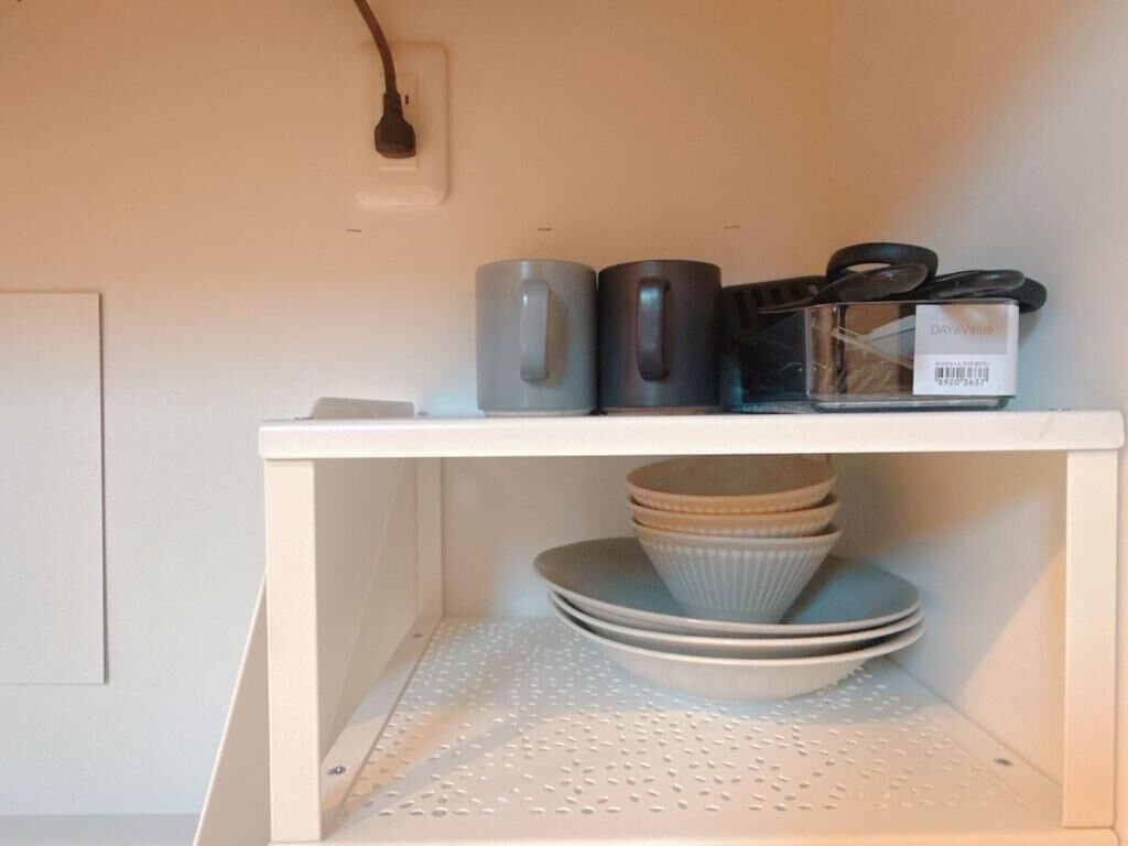 A kitchen shelf with a coffee maker, a kettle, and a set of plates.