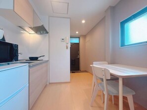 A modern kitchen with a microwave, stove, and cabinets. There is a dining area with a table and chairs. - Aoba Residence Designer Apartments 201 (大阪市)