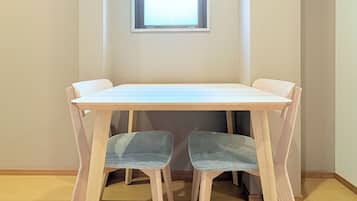 A room with a wooden table and two chairs, a window with blinds, and a towel rack.