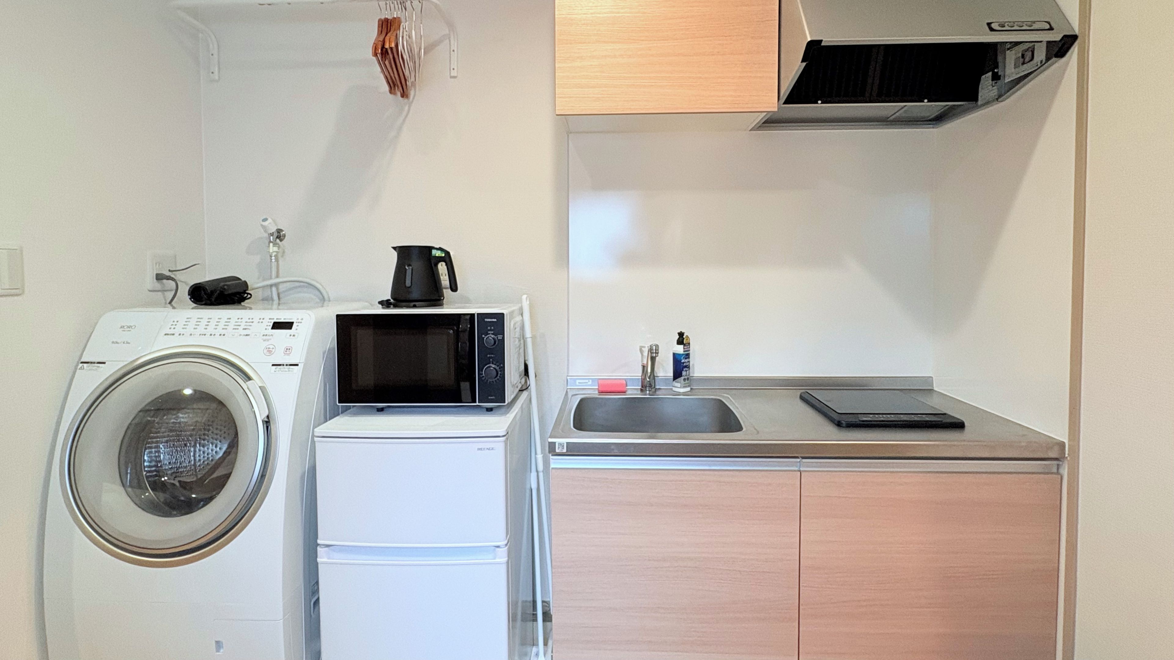 Un espace buanderie compact comprenant un lave-linge, un four à micro-ondes et un évier avec un plan de travail.