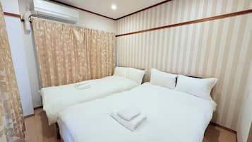 A hotel room with two beds, a window with curtains, an air conditioning unit, and striped wallpaper.