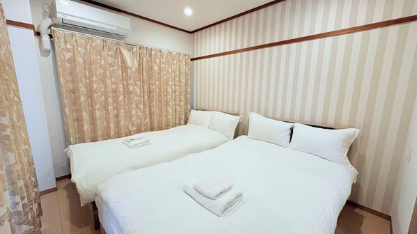 Une chambre d’hôtel avec deux lits, une fenêtre avec des rideaux, un appareil de climatisation et un papier peint à rayures.