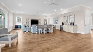 A spacious living area with a kitchen, a dining area with stools, a large flat-screen TV, and a ceiling fan. - Sea Y'all Soon - Oceanfront in Garden City Beach (Garden City Beach)